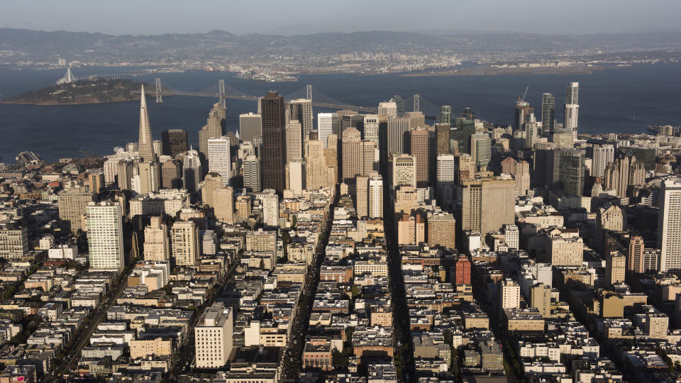 The Transamerica Pyramid building, left, stands in the skyline of downtown as the San Francisco-Oakland Bay Bridge crosses over Treasure Island in this aerial photograph taken above San Francisco, California, U.S., on Monday, Oct. 5, 2015. With tech workers flooding San Francisco, one-bedroom apartment rents have climbed to $3,500 a month, more than in any other U.S. city. Photographer: David Paul Morris/Bloomberg via Getty Images