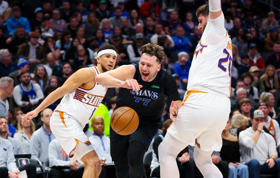 Dallas Mavericks guard Luka Doncic (77) drives to the basket as Phoenix Suns guard Devin Booker (1) and Phoenix Suns center Jusuf Nurkic (20) defend during the first half at American Airlines Center in Dallas, Texas on Jan. 24, 2024.