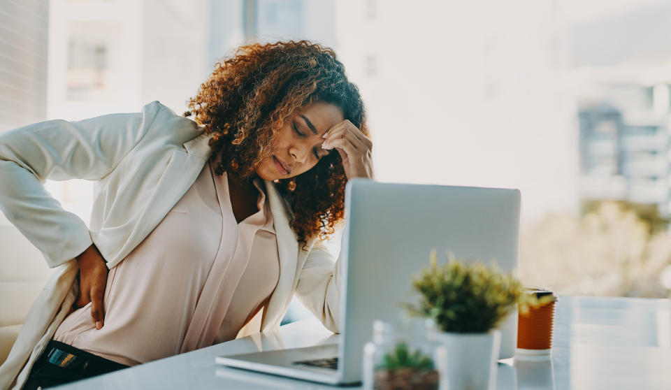 Shot of a young businesswoman experiencing back pain while working in a modern office