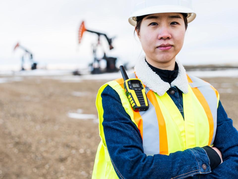 A person in protective gear with oil wells in the background.