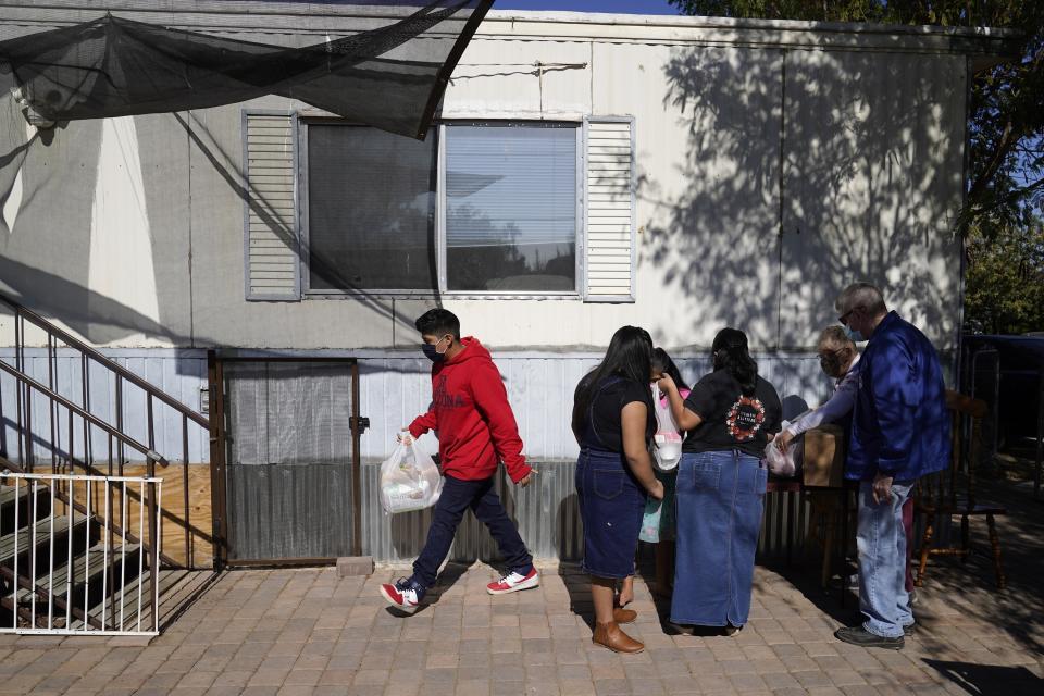 From left, Eliel Leocadio, 12, sisters Zeret, 10, Areli, 9, and their mother, Abigail Leocadio, bring food into their home after volunteers Mary Ann Kneip and her husband, Pete Kneip, from St. Vincent de Paul, make a delivery Saturday, Nov. 14, 2020, in Phoenix. When Abigail Leocadio's husband, a restaurant cook, was laid off earlier in the pandemic, her income _ barely more than the $11 state minimum wage _ wasn’t enough to cover their expenses. (AP Photo/Ross D. Franklin)