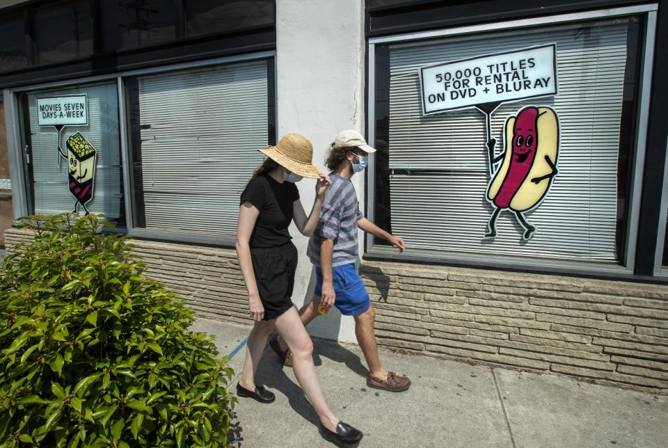 Pedestrians walk past windows with the shades down and an animated hot dog holding a sign advertising Vidiots' offerings.