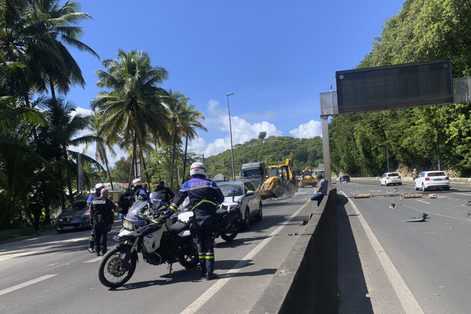 Police officers direct the traffic after protests on a road in Le Gosier, Guadeloupe island, Sunday, Nov.21, 2021. French authorities sent police special forces to the Caribbean island of Guadeloupe, an overseas territory of France, as protests over COVID-19 restrictions erupted into rioting and looting for the third day in a row. On Sunday, many road blockades by protesters made traveling across the island nearly impossible. (AP Photo/Elodie Soupama)