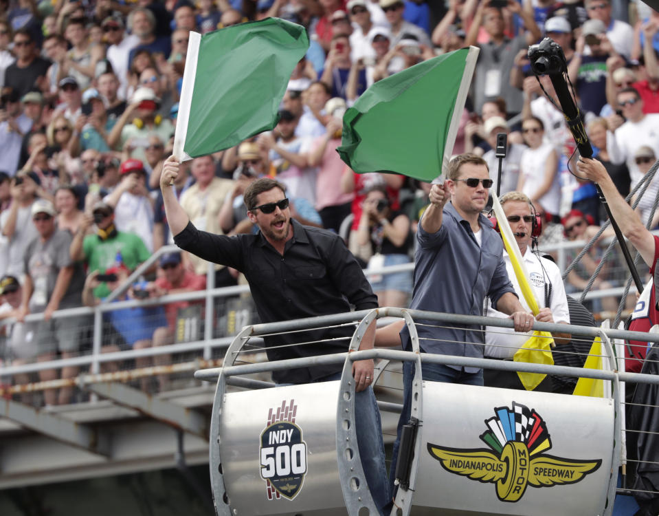 FILE - In this May 26, 2019, file photo, actors Christian Bale, left, and Matt Damon wave green flags to start Indianapolis 500 IndyCar auto race at Indianapolis Motor Speedway in Indianapolis. The Indianapolis 500 scheduled for May 24 has been postponed until August because of the coronavirus pandemic and won't run on Memorial Day weekend for the first time since 1946. The race will instead be held Aug. 23. (AP Photo/Michael Conroy)