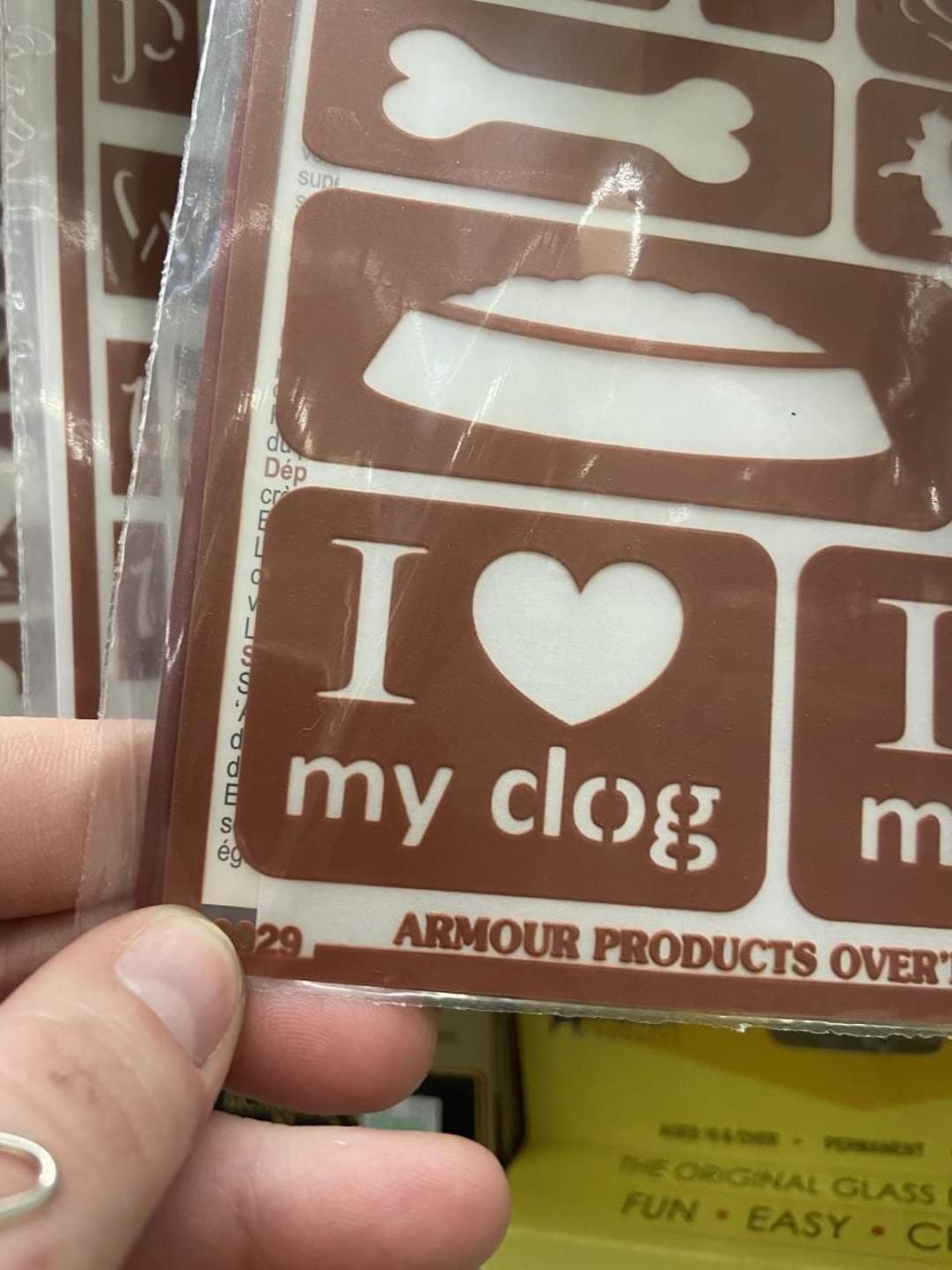 A person holding a stencil with the text "I ♥ my clog;" it's supposed to read "I ♥ my dog," but there's a space in the d