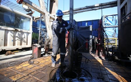A worker cleans a drilling rig covered with mug at Vaca Muerta shale oil and gas drilling, in the Patagonian province of Neuquen