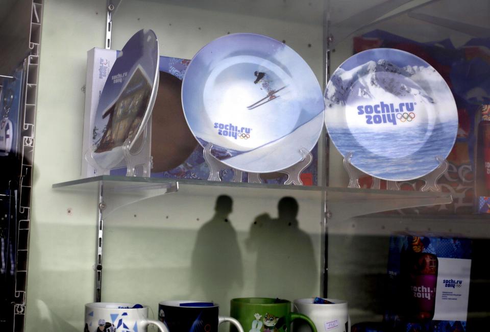 Olympic souvenir plates are displayed in a shop as pedestrians are reflected in the window while strolling along a boardwalk on the Black Sea, Wednesday, Jan. 29, 2014, in Sochi, Russia, home of the upcoming 2014 Winter Olympics. (AP Photo/David Goldman)