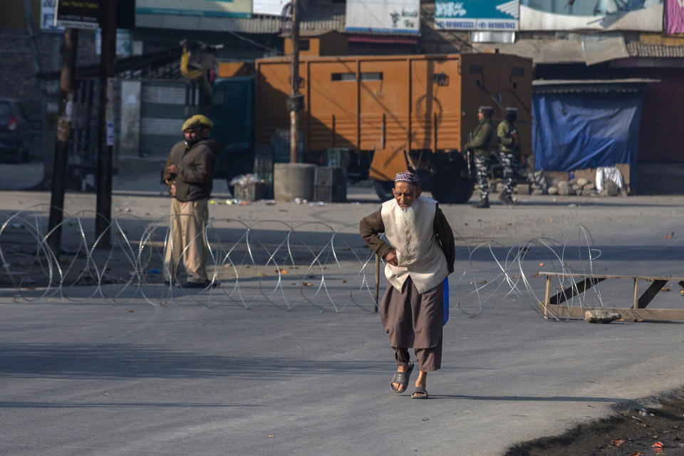 An elderly Kashmiri man walks past barbed wire set up as road blockade by soldiers on a road leading towards the site of a gunfight in Pampore, south of Srinagar, Indian controlled Kashmir, Saturday, Oct. 16, 2021. Indian government forces killed five rebels in last 24-hours in disputed Kashmir on Saturday, officials said, as violence increased in recent weeks. (AP Photo/Dar Yasin)