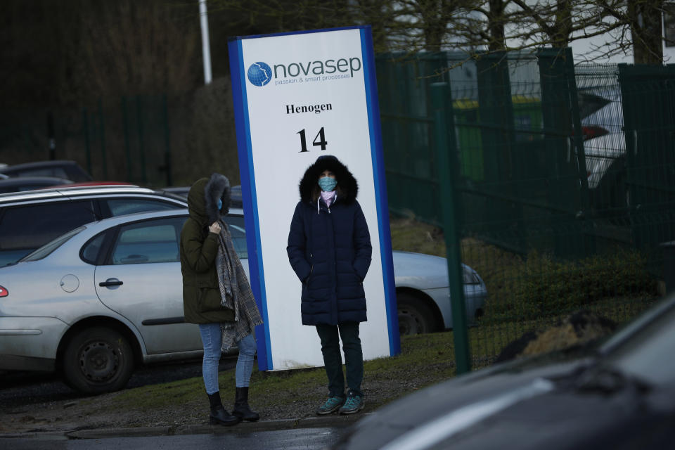 People, wearing face masks to prevent the spread of the coronavirus, stand next to the entrance of the Novasep factory in Seneffe, Belgium, Friday, Jan. 29, 2021. The European Union has made public a redacted version of the contract it agreed with the drugmaker AstraZeneca which lies at the heart of a major row over coronavirus vaccine deliveries. (AP Photo/Francisco Seco)