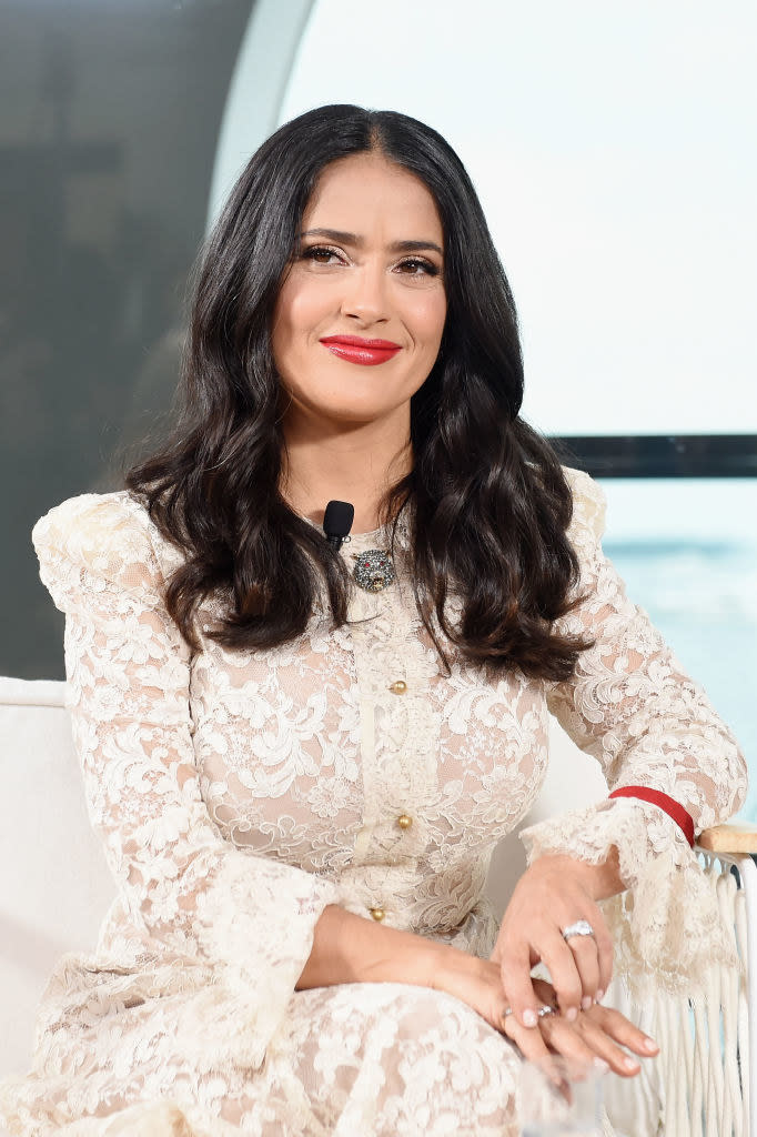 A smiling Salma seated and wearing a long-sleeved lacy dress