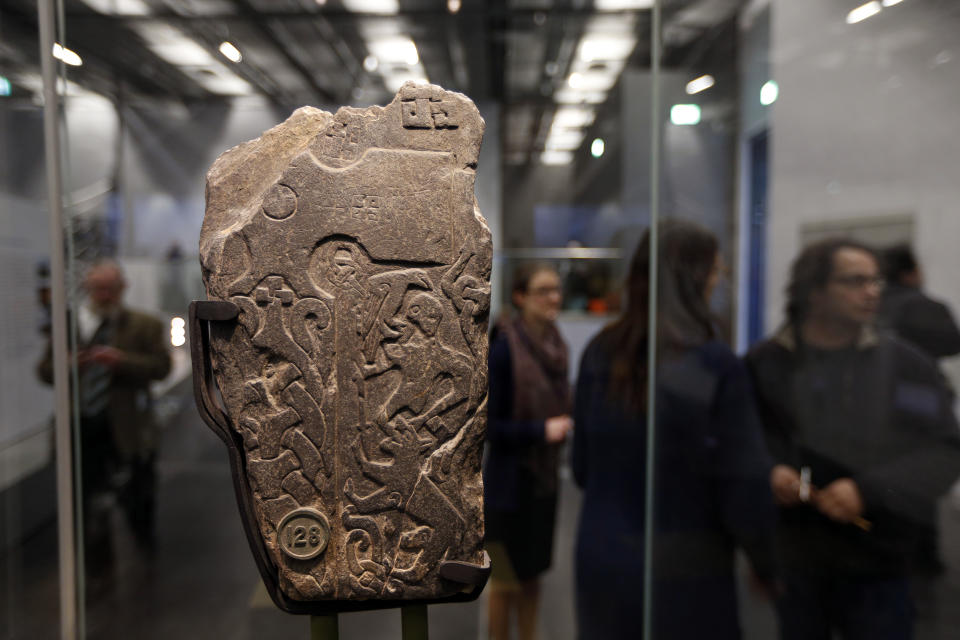 Visitors walk past a fragment of a Viking engraved stone as they view a new exhibition entitled 'Vikings: Life and Legend' at the British Museum in central London, Tuesday, March 4, 2014. The new exhibition strives to make people think again about the Scandinavian pillagers who raided and struck terror into English villages. The exhibition aims to show how Viking energy and ideas re-drew the map of the world, through the presentation of their ships, their weapons, their crafts, their words and even their skeletons. (AP Photo/Lefteris Pitarakis)