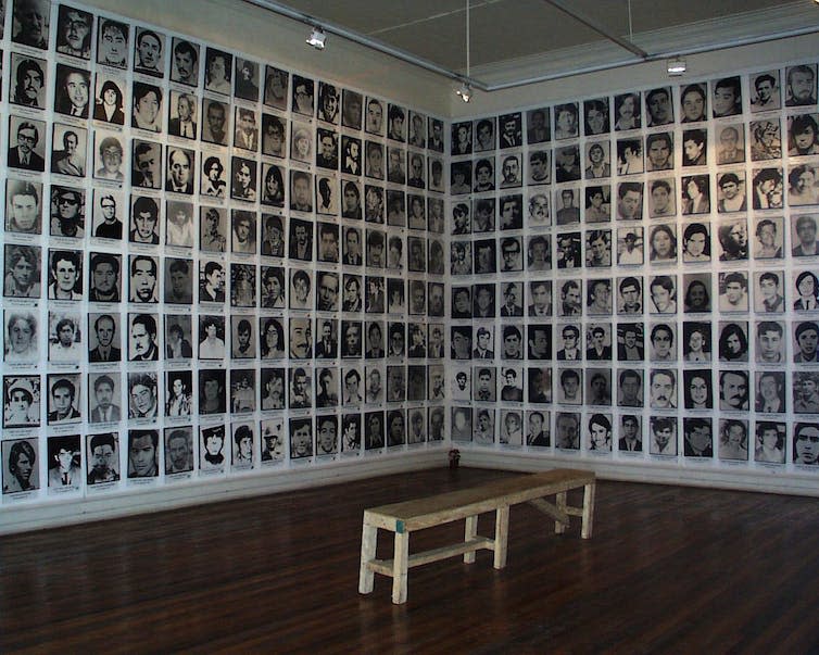 Una pared de fotografías de rostros en blanco y negro en una galería.
