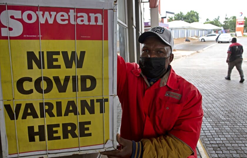 A petrol attendant stands next to a newspaper headline in Pretoria, South Africa, Saturday, Nov. 27, 2021. As the world grapples with the emergence of the new variant of COVID-19, scientists in South Africa — where omicron was first identified — are scrambling to combat its spread across the country. (AP Photo/Denis Farrell)