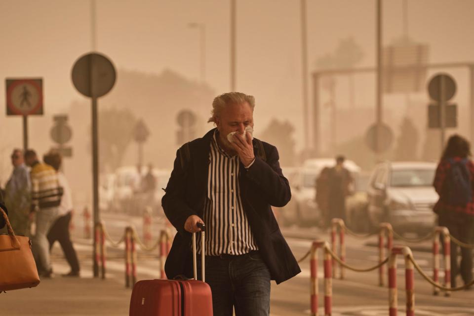 A passenger covers his nose and mouth in a cloud of red dust at the airport in Santa Cruz de Tenerife, Spain, Sunday, Feb. 23, 2020.