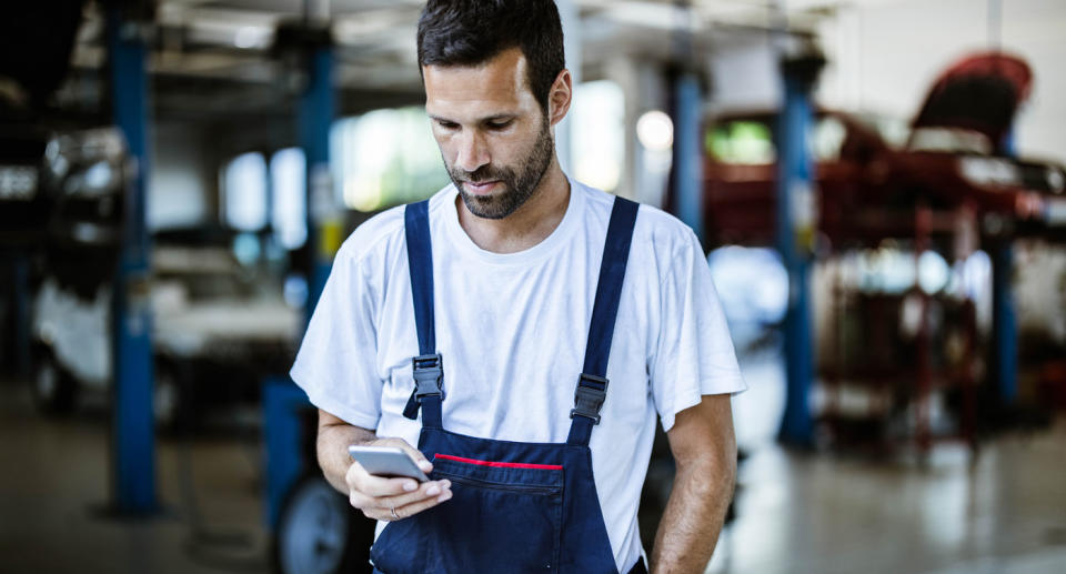 Man texts in a mechanics workshop.