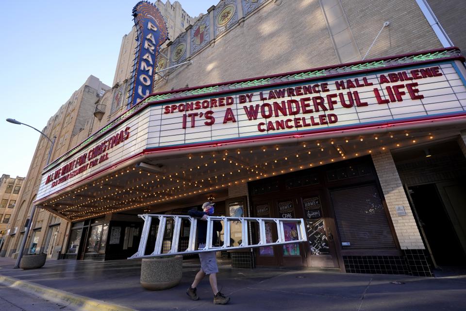 Employee Grayson Allred walks away with a ladder after working on the front marquee at the Paramount Theatre on Wednesday, Dec. 16, 2020, in Abilene, Texas. The marquee which in part reads, "It's A Wonderful Life, Cancelled", notifies all would-be patrons that the theatre has closed down indefinitely due to rising cases of COVID-19 in the city. (AP Photo/Tony Gutierrez)