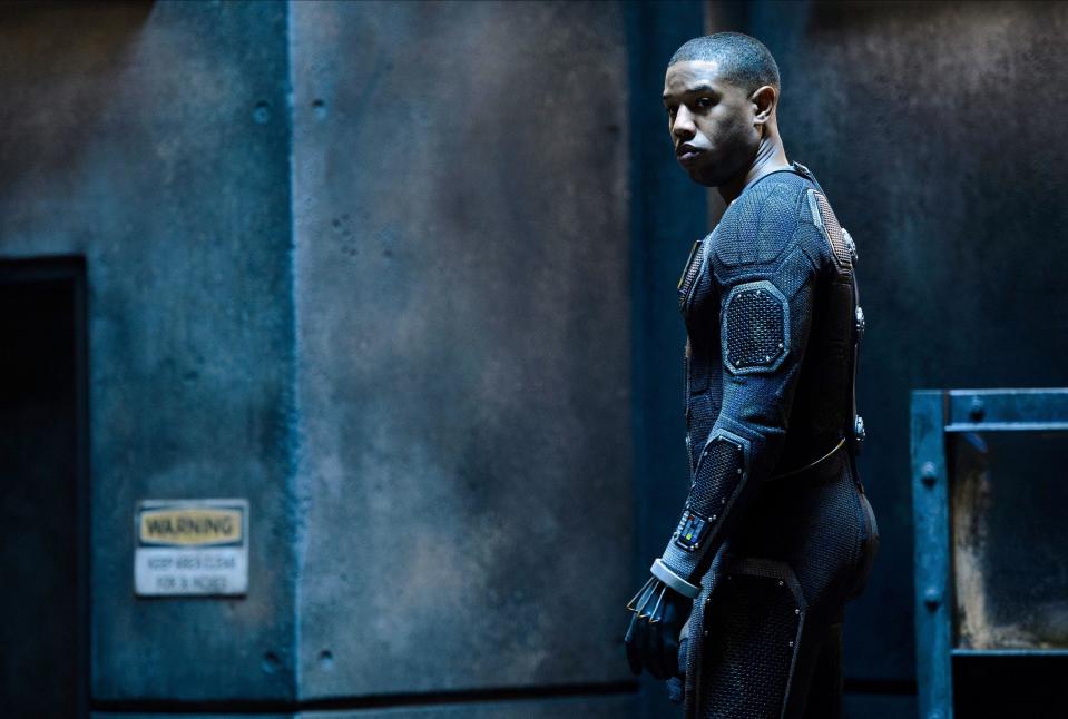 A man in a skin tight semi-mechanical suit stands alone in an industrial setting