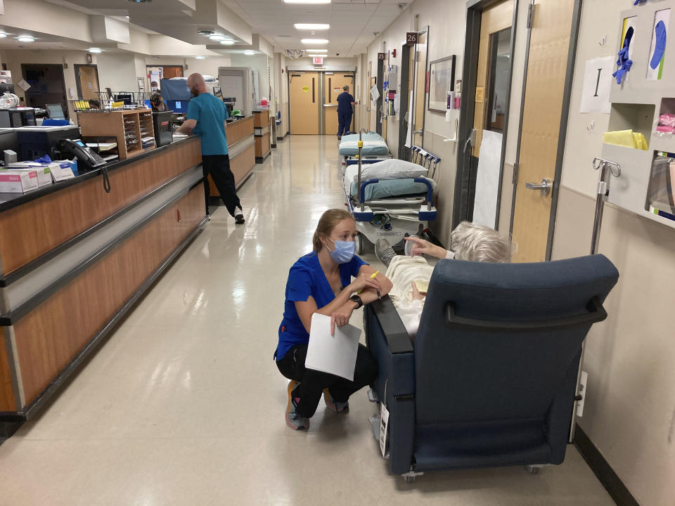 FILE - In this Aug. 20, 2021, file photo, a nurse talks to a patient in the emergency room at Salem Hospital in Salem, Ore., with gurneys lining the hallway behind them, ready to take patients if needed. Gov. Kate Brown announced Wednesday, Aug. 25, 2021, that the state has contracted with a medical staffing company to provide up to 500 health care workers to hospitals around the state to help respond to the surge in patients due to the delta variant. (AP Photo/Andrew Selsky, File)