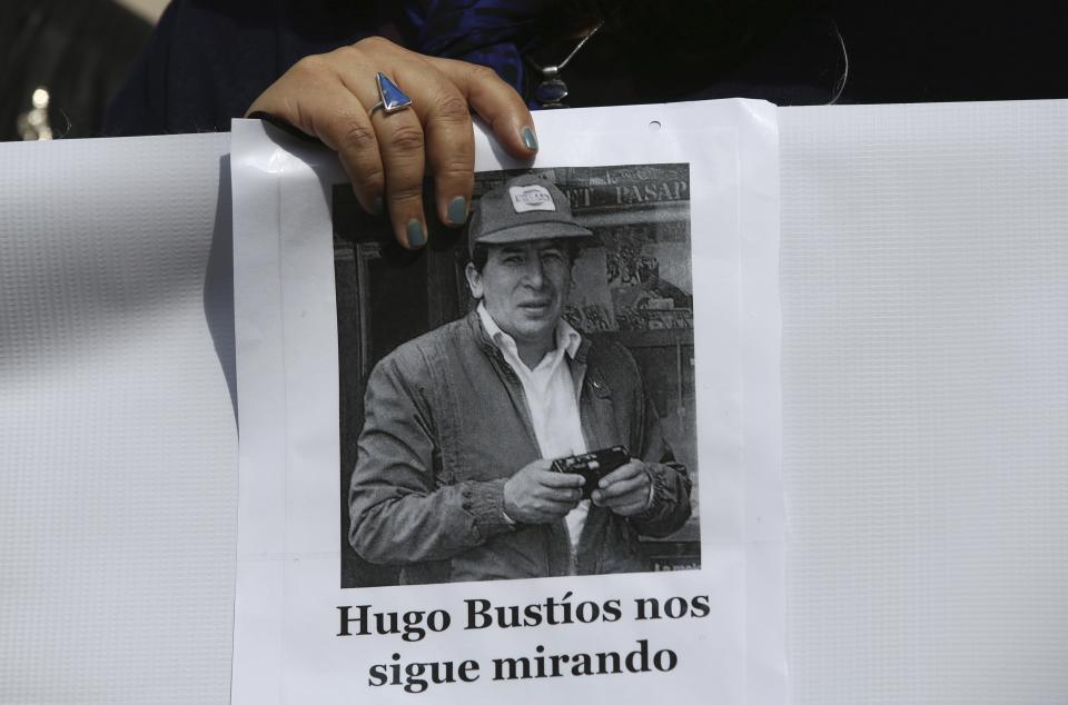 A protester holds a photo of Hugo Bustíos, who is wearing a baseball cap and carrying what appears to be a disposable camera, accompanied by a text in Spanish that translates as: 