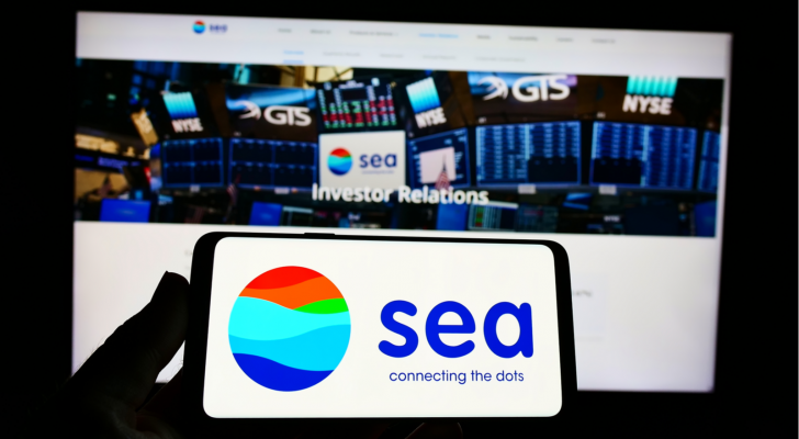 Person holding cellphone with logo of Singaporean technology conglomerate Sea Ltd on screen in front of business webpage Focus on phone display. SE stock