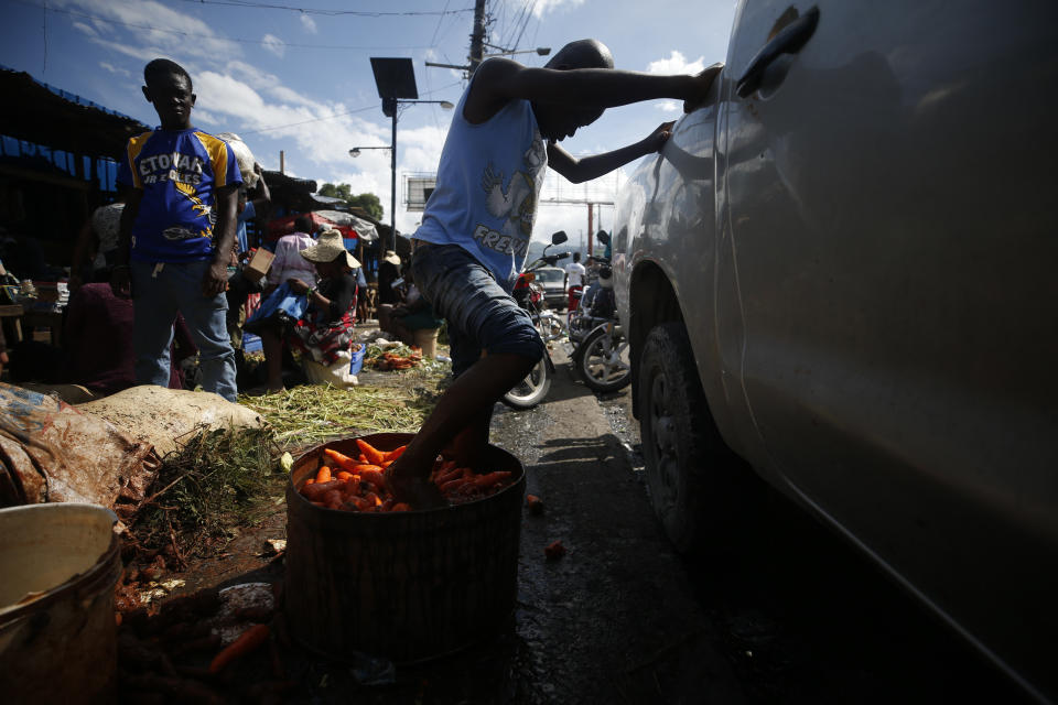 A youth cleans carrots by agitating them with his feet in a tub of murky water, at a market in Petionville, Port-au-Prince, Haiti, Wednesday, Oct. 2, 2019. There was a relative pause Wednesday in disturbances that have wracked Haiti's capital for weeks as protesters have tried to drive President Jovenel Moïse from power. (AP Photo/Rebecca Blackwell)
