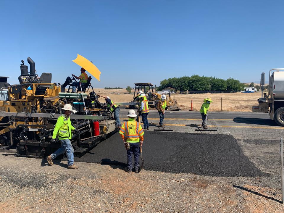 TechniSoil workers get the newly repaved road ready before the steam roller flattens it.