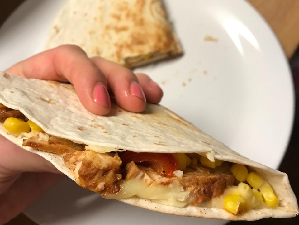 A hand holding a chicken, cheese and sweetcorn quesadilla.