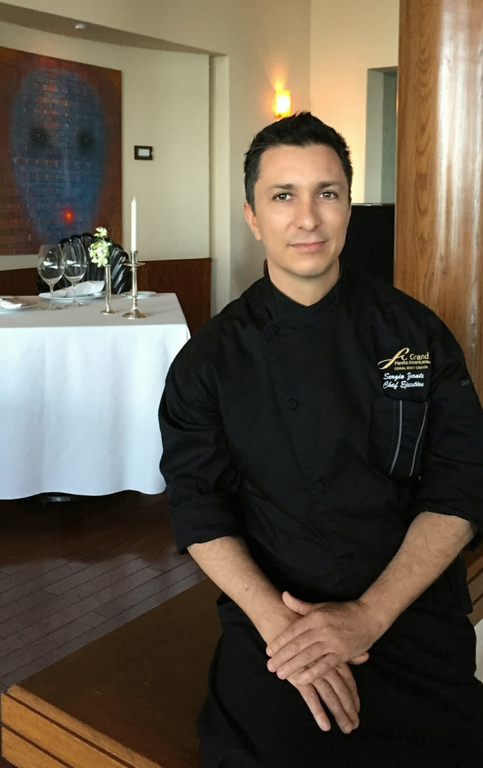 Chef Sergio Zárate sits inside a Grand Fiesta Americana restaurant, wearing a hotel-branded black chef's uniform.