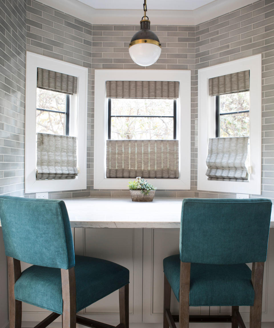 Breakfast bat area in bay window with two bar stools, three windows dressed in blinds, rounded glass pendant hanging above