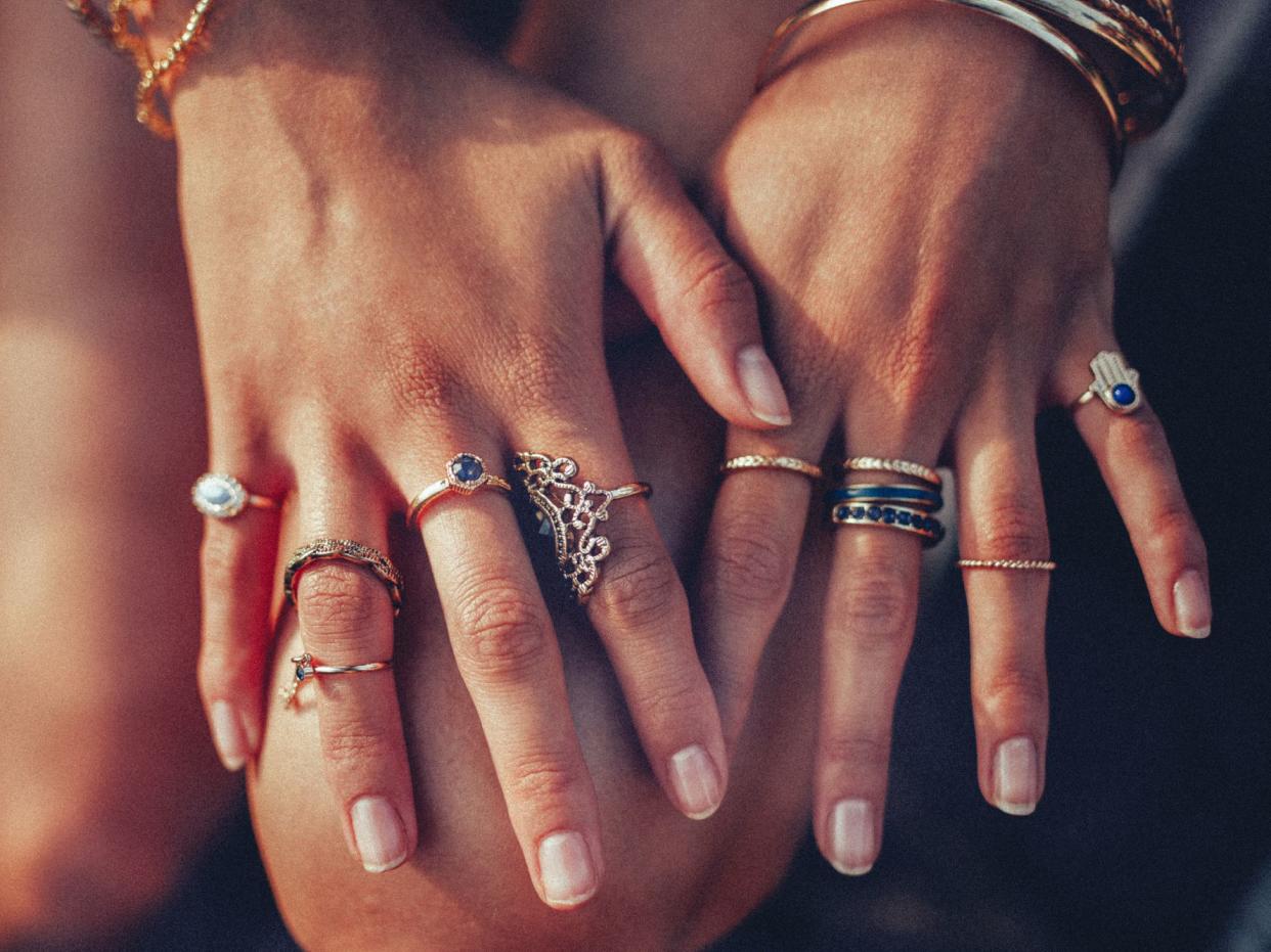 Cropped closeup of a boho girl's hands with many rings on her fingers, in gold and silver with dark blue stones