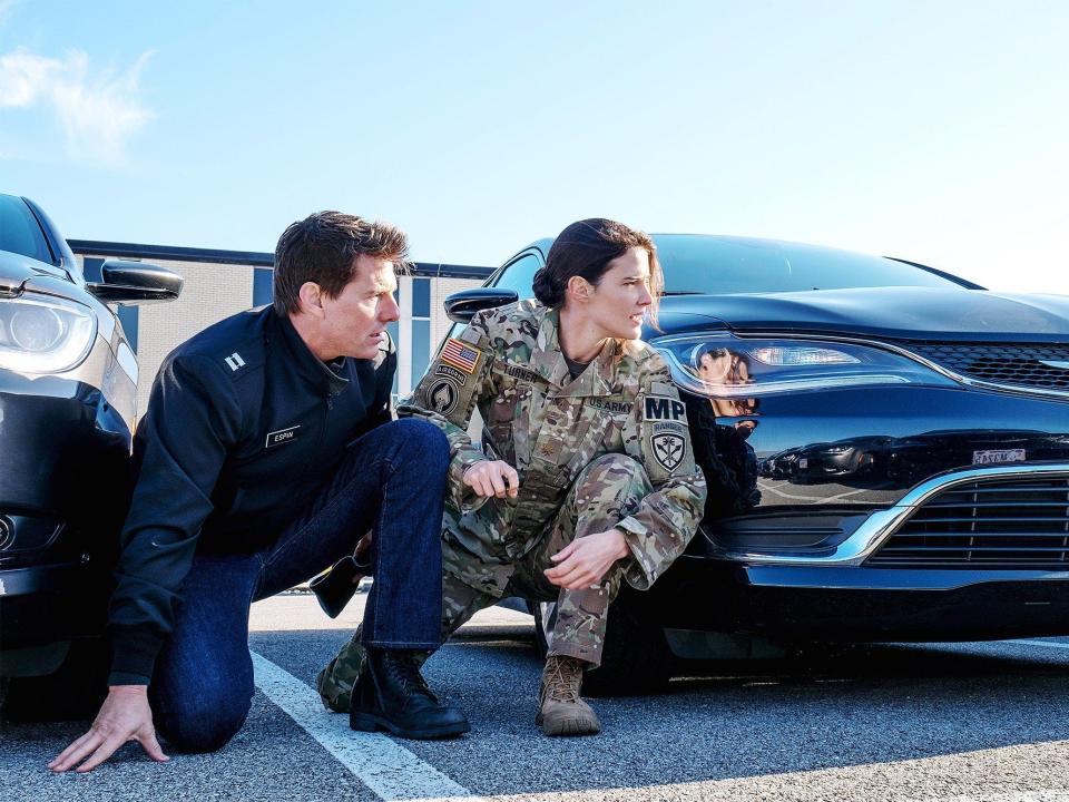 Tom Cruise and Cobie Smulders in "Jack Reacher: Never Go Back" crouching next to a car