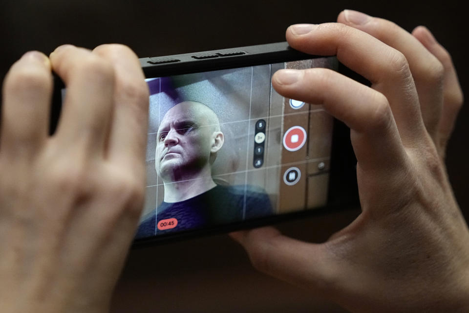 Sergei Udaltsov, Russian left-wing political activist is seen on a phone's screen as he stands behind a glass in a cage in a courtroom in Moscow, Russia, Friday, Jan. 12, 2024. Sergei Udaltsov, a Russian pro-war activist and critic of President Vladimir Putin, was remanded into custody Thursday over alleged terrorism offenses, his lawyer told the Russian state news agency Tass. (AP Photo/Alexander Zemlianichenko)