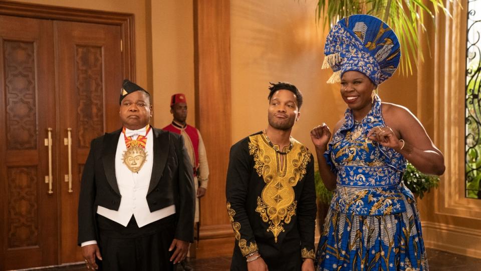 A woman wearing African clothing and a hat stands next to two men in African clothing