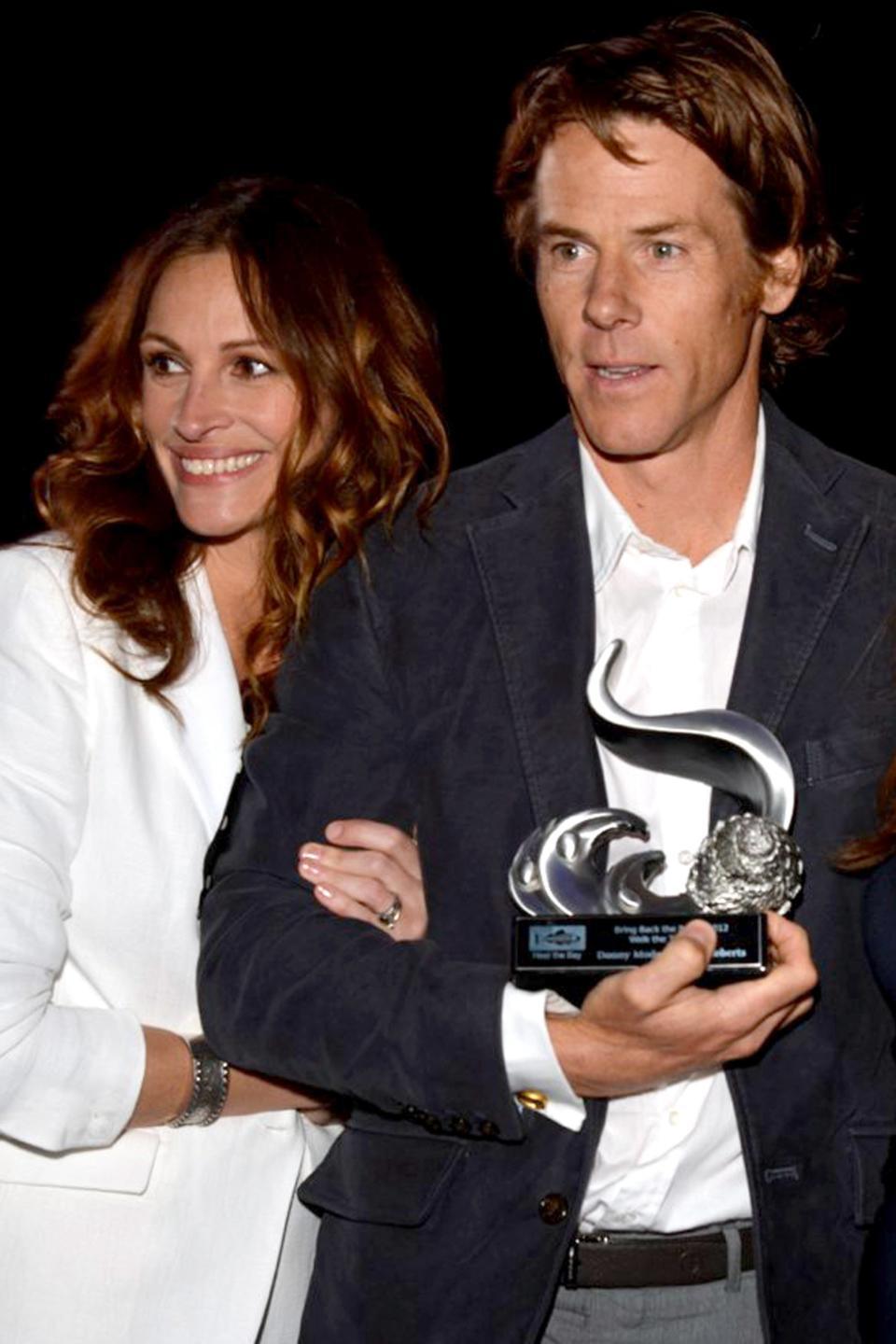 Julia Roberts and Daniel Moder holding an award at a ceremony. Julia Roberts is wearing a stylish suit