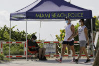 People wearing protective face masks walk past a closed entrance to the beach during the new coronavirus pandemic, Friday, July 3, 2020, in the South Beach neighborhood of Miami Beach, Fla. Beaches throughout South Florida are closed for the busy Fourth of July weekend to avoid further spread of the new coronavirus. (AP Photo/Lynne Sladky)