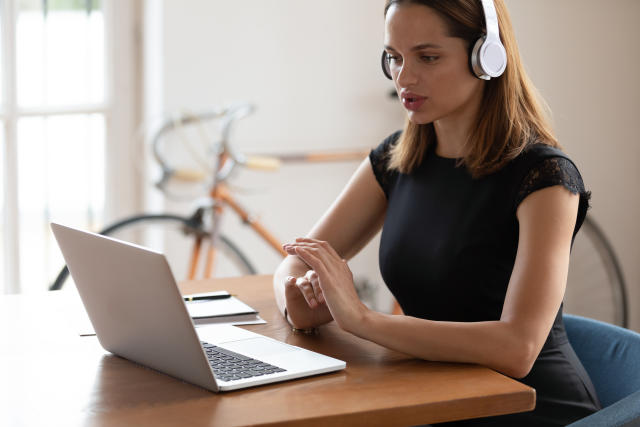 Side view concentrated businesswoman wearing wireless headphones, listening to educational seminar at workplace. Young confident female entrepreneur manager worker holding video call with clients.
