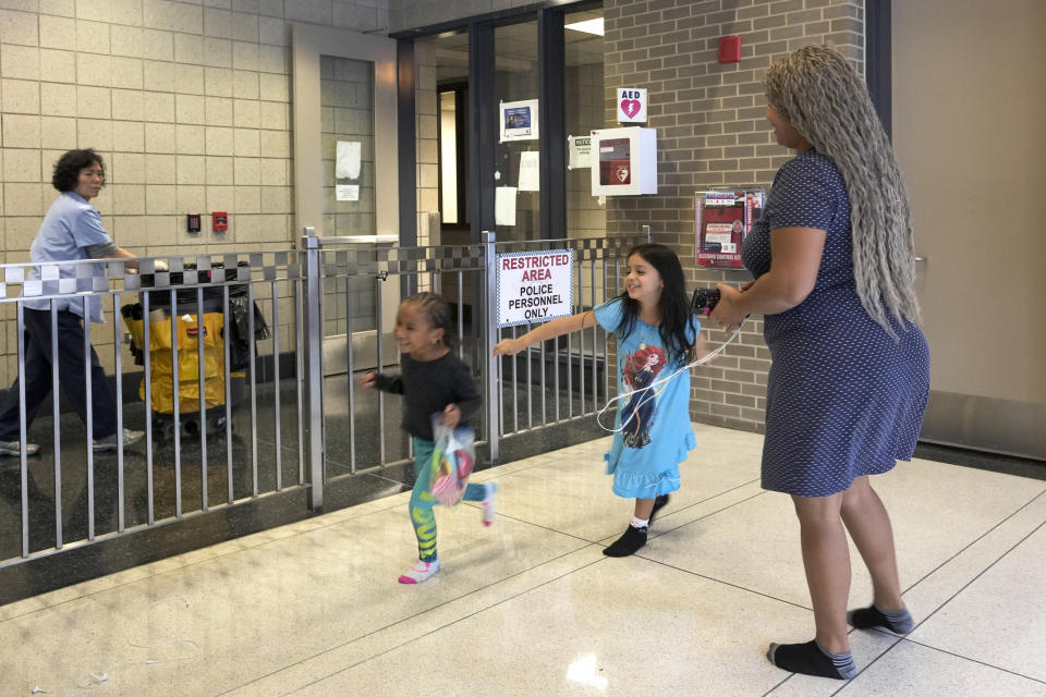 Yessika Chirino, an immigrant from Venezuela plays with her daughter Charlotte, left, and Avril Brandelli as they take shelter in the Chicago Police Department's 16th District station on Monday, May 1, 2023. Chicago has seen the number of new arrivals grow tenfold in recent days. Shelter space is scarce and migrants awaiting a bed are sleeping on floors in police stations and airports. (AP Photo/Charles Rex Arbogast)