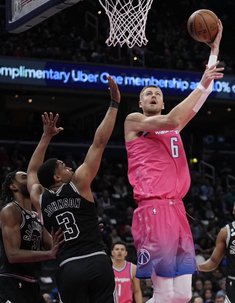 Washington Wizards center Kristaps Porzingis (6) goes up to shoot over San Antonio Spurs forward Keita Bates-Diop (31), and forward Keldon Johnson (3), during the first half of an NBA basketball game Friday, March 24, 2023, in Washington. (AP Photo/Carolyn Kaster)