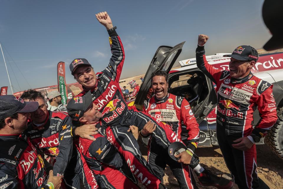 Driver Carlos Sainz, of Spain, center, is lifted by Driver StÈphane Peterhansel, of France, center and left, and driver Nasser Al-Attiyah, of Qatar, center and right, at the end of stage twelve of the Dakar Rally between Haradth and Qiddiya, Saudi Arabia, Friday, Jan. 17, 2020. (AP Photo/Bernat Armangue)