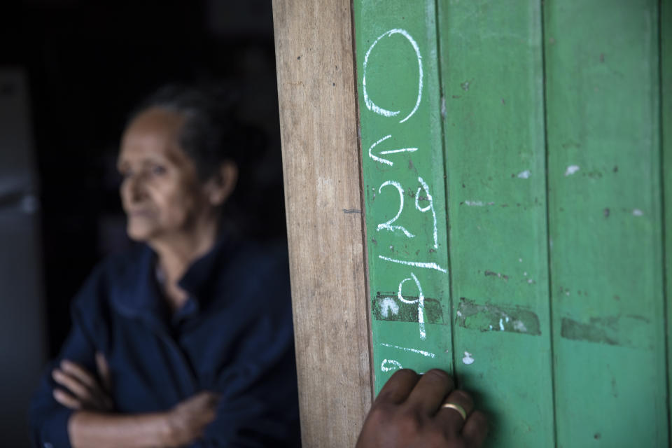 Leila Ramirez, who is suffering from dengue, stands in her doorway as a member of the campaign against dengue documents their visit on the wood siding of her home, in Pucallpa, in Peru's Ucayali region, Tuesday, Sept. 29, 2020. Five members in Ramirez's family were diagnosed with dengue in late September, but have since recovered. In recent weeks, health officials have reported over 33,000 dengue cases, concentrated largely in the Amazon. (AP Photo/Rodrigo Abd)