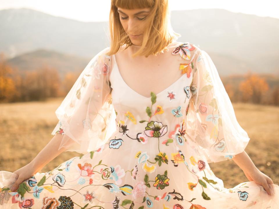 A bride holds out her flower covered dress in a field.