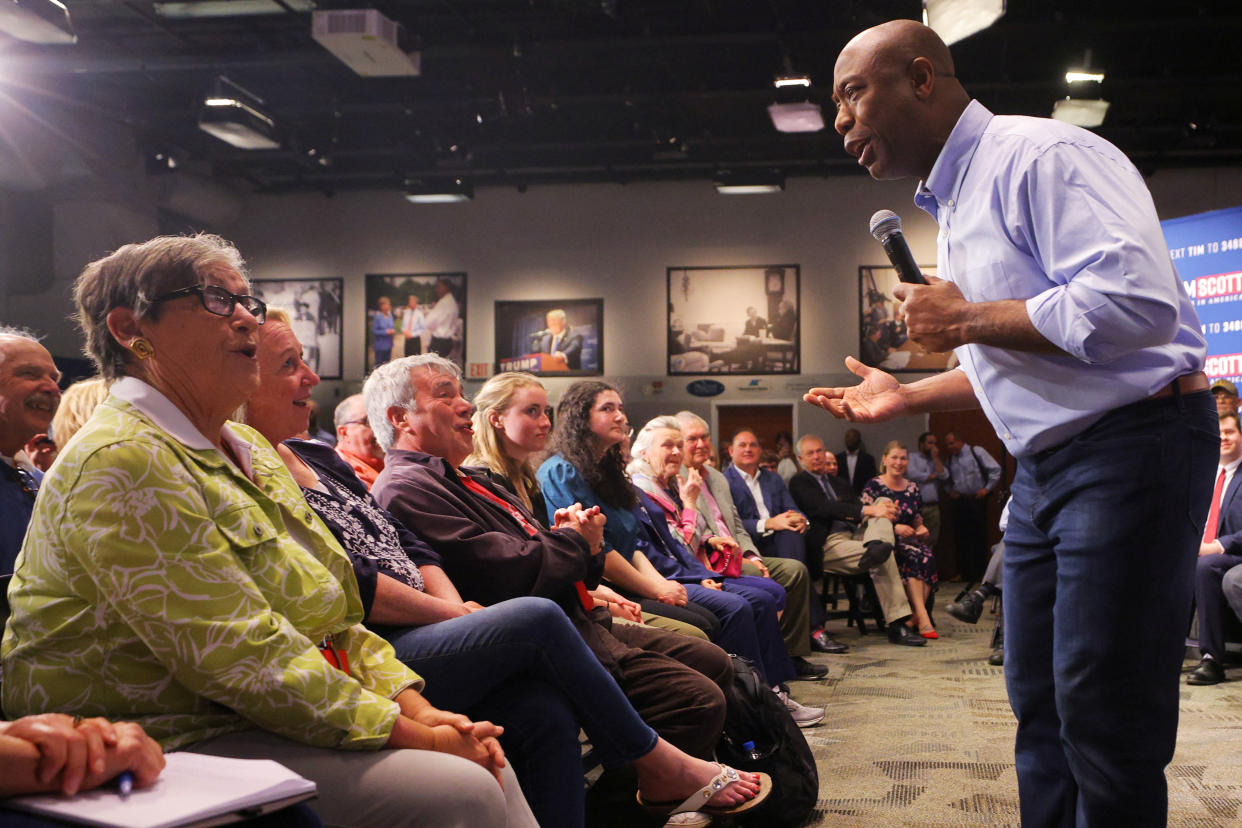 Scott, standing in the front row of his audience with a microphone, bends forward to talk to a row of middle-aged white audience members.