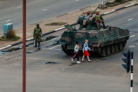 <p>Young women walk past an armoured personnel carrier that stations by an intersection as Zimbabwean soldiers regulate traffic in Harare on Nov. 15, 2017. (Photo: AFP/Getty Images) </p>