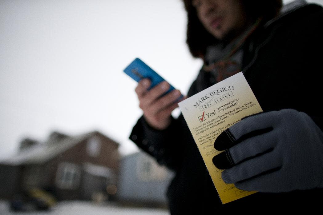 In this Oct. 9, 2014 photo, campaign worker Gabe Tegoseak makes a note on a list of voters he keeps on his phone as he gets a promise card to vote for Sen. Mark Begich from a resident while canvassing in Barrow, Alaska. Democrats hope to benefit from the addition of nearly 130 early voting sites this year, nearly all in rural communities that in the past had to mail-in ballots, or fly or drive to another community. (AP Photo/Gregory Bull)