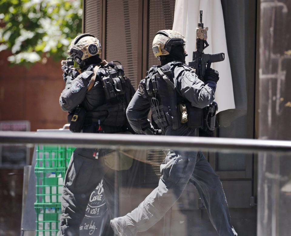 A police officer runs across Martin Place near Lindt cafe, where hostages are being held, in central Sydney December 15, 2014. Hostages were being held inside the central Sydney cafe where a black flag with white Arabic writing could be seen in the window, local television showed on Monday, raising fears of an attack linked to Islamic militants. REUTERS/David Gray (AUSTRALIA - Tags: CRIME LAW CIVIL UNREST)