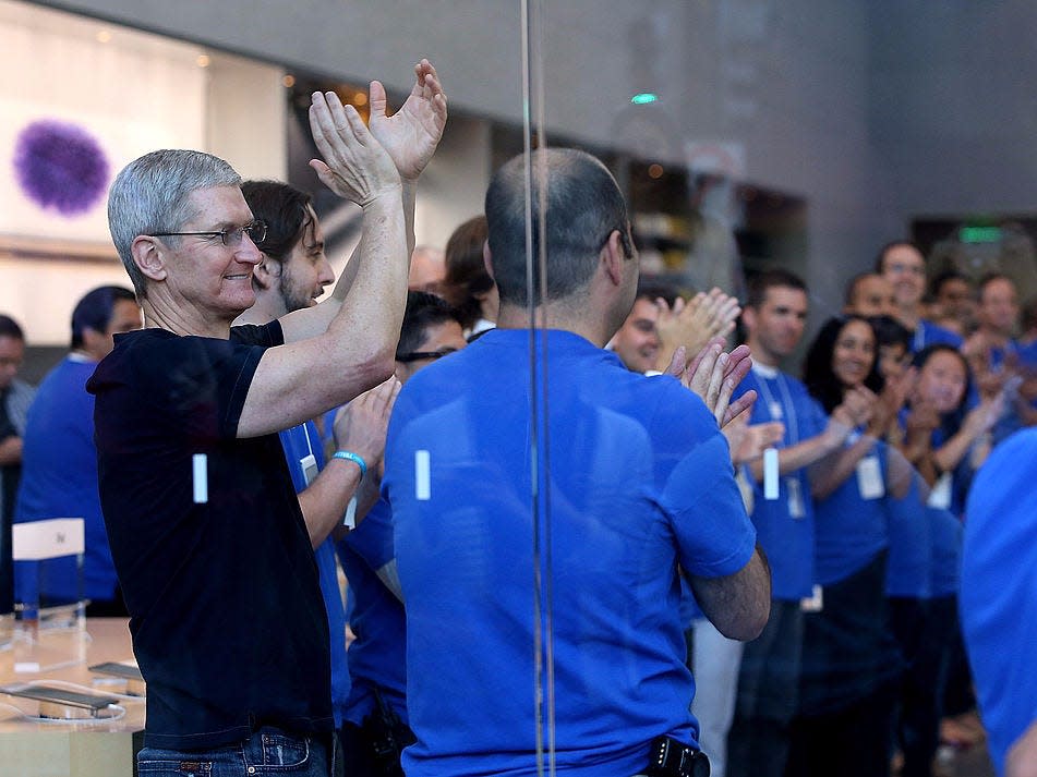 Tim Cook raising his hands and clapping among a group of Apple workers.