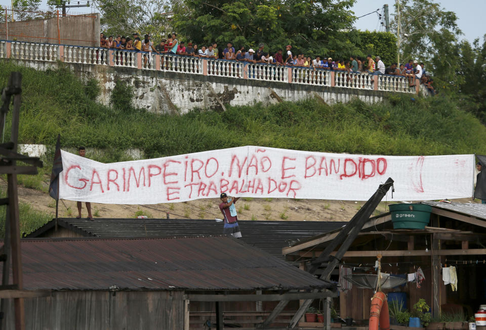 Illegal miners display a banner that reads in Portuguese "Gold miners are not bandits, They are workers," after more than 60 dredging barges were set on fire by officers of the Brazilian Institute of the Environment and Renewable Natural Resources, IBAMA, during an operation to try to contain illegal gold mining on the Madeira river, a tributary of the Amazon river in Borba, Amazonas state, Brazil, Sunday, Nov. 28, 2021. Hundreds of barges belonging to illegal miners had converged on the river during a gold rush in the Brazilian Amazon prompting IBAMA authorities to start burning them. (AP Photo/Edmar Barros)