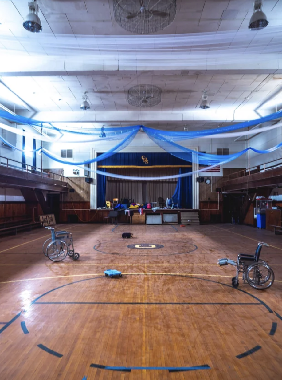 The gym's ceiling is still decorated, but it is otherwise empty except for two wheelchairs, giving it an eerie feeling