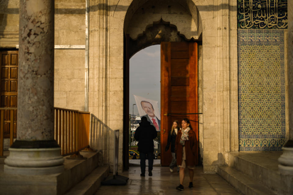 People step in Yeni mosque next to a campaign banner of Turkish President and leader of the Justice and Development Party, or AKP, Recep Tayyip Erdogan, in Istanbul, Turkey, Saturday, March 16, 2024. With local elections across Turkey days away, legal experts are coaching thousands of volunteer election monitors on the rules they'll need to watch for fraud and ensure a fair vote. (AP Photo/Emrah Gurel)