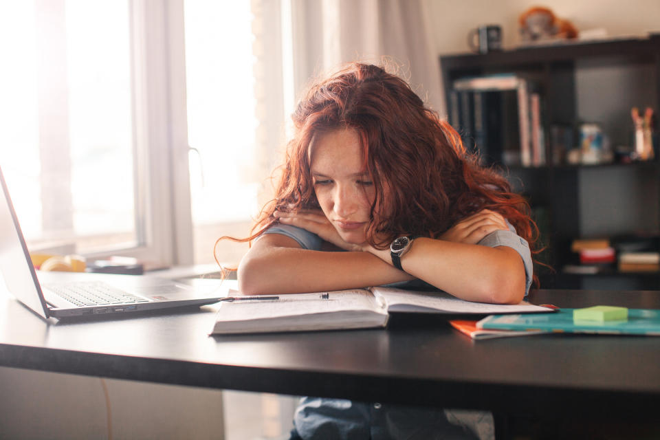 student with a very sad expression and an open textbook and laptop